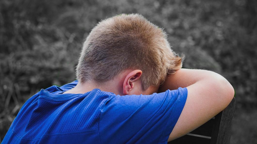 Een jongen staat huilend met zijn hoofd in zijn armen